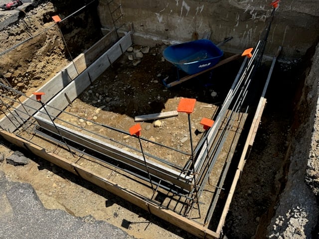 Concrete foundation with rebar framework and wheelbarrow in construction site, illustrating masonry repair process for structural integrity.