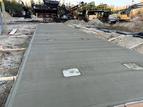 Concrete slab in construction site with machinery and materials in background, illustrating poured concrete work for masonry repair services.