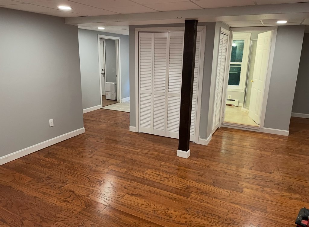 Bright, renovated basement living area featuring hardwood flooring, gray walls, and a closet, showcasing functional upgrades and maximizing natural light.