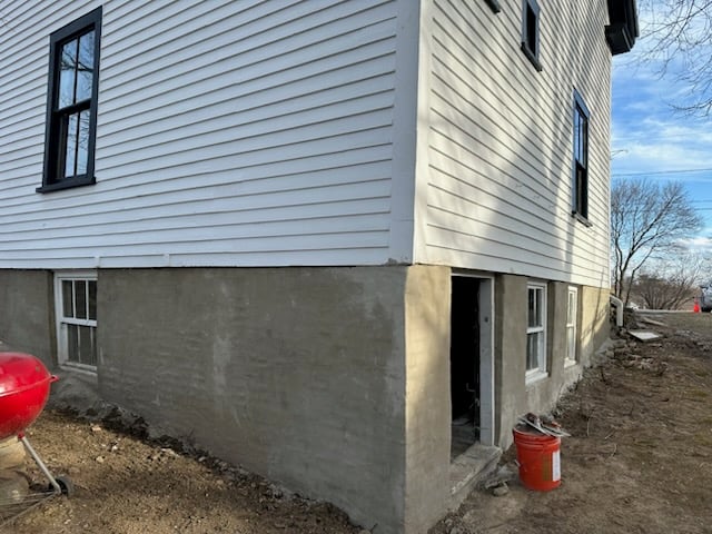 Concrete foundation repair on a residential building, showcasing freshly applied concrete at the base, adjacent to white siding and windows, highlighting masonry restoration efforts.